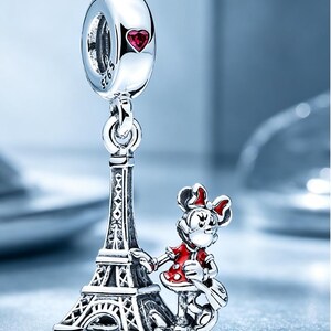 Puede incluir: Un charm de plata que presenta una torre Eiffel en miniatura y un personaje de rat&oacute;n de dibujos animados con vestido y lazo rojos. El asa superior tiene grabado S925 y un peque&ntilde;o coraz&oacute;n rojo. El dise&ntilde;o est&aacute; hecho en plata pulida.
