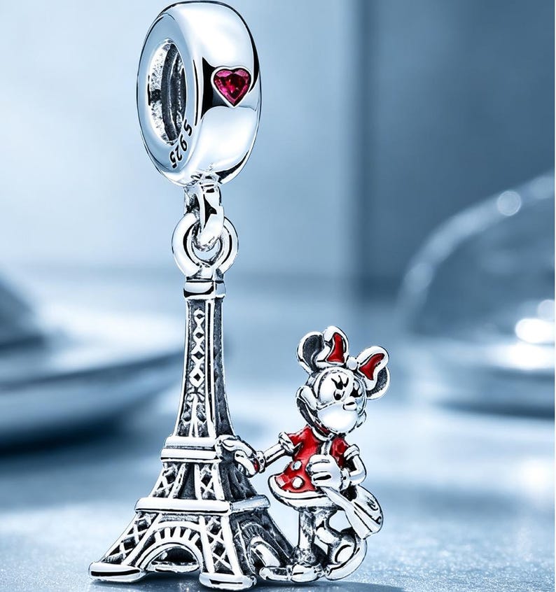 Puede incluir: Un charm de plata que presenta una torre Eiffel en miniatura y un personaje de rat&oacute;n de dibujos animados con vestido y lazo rojos. El asa superior tiene grabado S925 y un peque&ntilde;o coraz&oacute;n rojo. El dise&ntilde;o est&aacute; hecho en plata pulida.