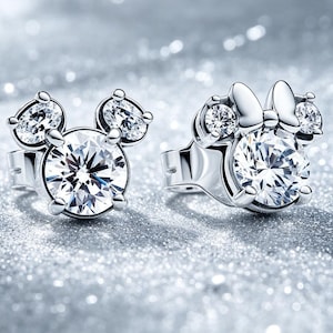 May include: A pair of silver-toned stud earrings featuring clear, round-cut stones. One earring is shaped like a mouse head with two smaller circular stones as ears, while the other includes a small bow detail above the central stone.