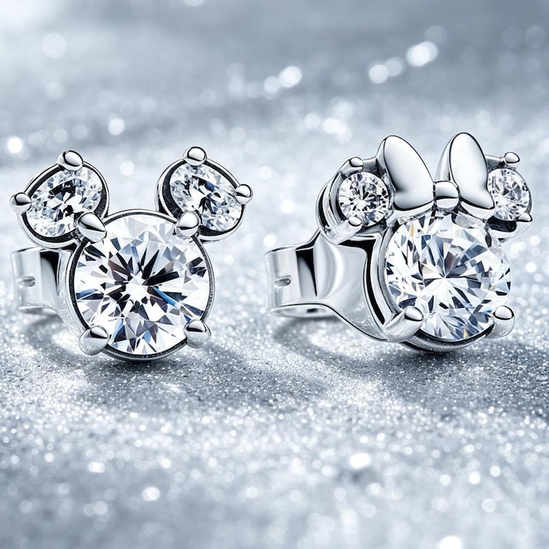 May include: A pair of silver-toned stud earrings featuring clear, round-cut stones. One earring is shaped like a mouse head with two smaller circular stones as ears, while the other includes a small bow detail above the central stone.
