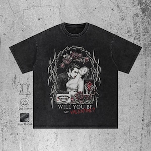 Flat lay of a premium black t-shirt featuring a dark romance vampire graphic. The shirt has a textured washed and a relaxed streetwear fit. The central print depicts a vampire biting a woman's neck, framed by withered roses and sharp cyber sigilism tribal thorns. Below the illustration, grunge text in white and blood red reads "WILL YOU BE MY VALENTINE?". The image shows the full shirt cut and the texture of the fabric clearly against a white background.