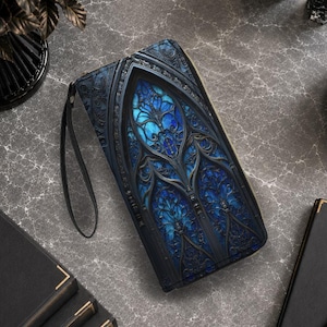 Puede incluir: Una cartera rectangular con cremallera que presenta un diseño de arco gótico oscuro y ornamentado, con intrincados patrones de filigrana negra sobre un efecto de vidriera azul brillante y luminoso. La cartera incluye una correa de muñeca negra.