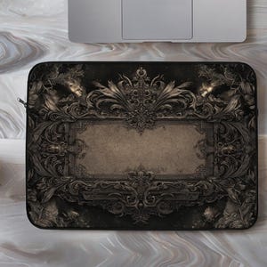 May include: Black laptop sleeve featuring an ornate, vintage-style design. The dark gray sleeve has a central rectangular panel framed by elaborate scrollwork and floral motifs. A zipper is visible on the side. A laptop and a potted succulent are in the background.
