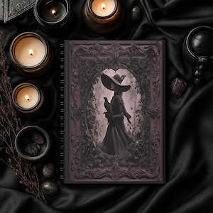May include: A spiral-bound notebook with a dark, gothic illustration of a woman in a wide-brimmed hat holding a bird. The notebook is surrounded by lit candles in ornate holders, small bowls with stones, and other dark-themed accessories, all on a black satin surface.
