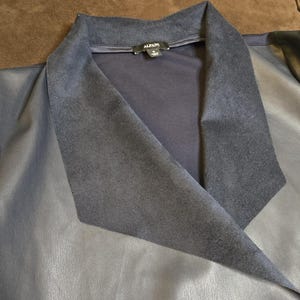 May include: A close-up of a navy blue jacket with a suede-like collar. The jacket has a leather-like texture and the tag reads "Alfani". The collar is a darker shade of blue than the rest of the jacket.