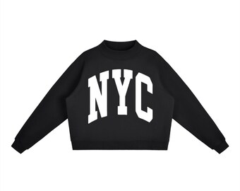Op de afbeelding: Zwart, kort sweatshirt met de witte letters "NYC" over de borst. De sweatshirt heeft een col en lange mouwen. De afbeelding is tegen een witte achtergrond.
