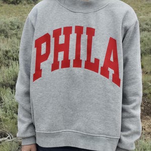 Front view of a gray oversized PHILA mockneck sweatshirt worn outdoors.