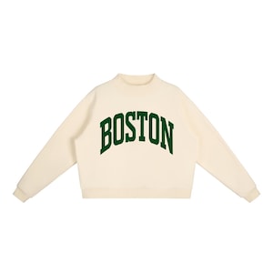 Op de afbeelding: Een cr&egrave;mekleurig sweatshirt met lange mouwen, een opstaande kraag en geribbelde boorden. Het woord BOSTON staat in een donkergroen, gebogen lettertype in collegestijl op de borst gedrukt. Het kledingstuk heeft een rechte zoom en lange mouwen.