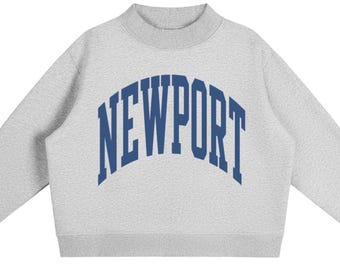 May include: A light grey long-sleeve sweatshirt with a mock neck collar and ribbed cuffs. The front features the word NEWPORT printed in a large, arched, dark blue collegiate-style font across the chest area of the garment.