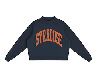 May include: A navy blue long-sleeve sweatshirt featuring a mock neck collar and ribbed cuffs. The word SYRACUSE is printed in a bold, arched orange font across the centre of the chest. The garment has a straight hemline and a solid dark base.