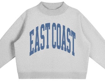 May include: A light grey long-sleeve sweatshirt with a mock neck collar and ribbed cuffs. The front features the text EAST COAST printed in a bold, arched, blue collegiate-style font across the chest area, centred on the heathered fabric.