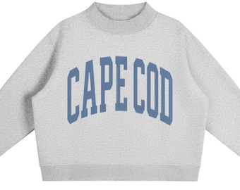 May include: A light grey long-sleeve sweatshirt with a mock neck collar and ribbed cuffs. The front features the text CAPE COD printed in a large, arched, blue collegiate-style font across the chest, centred on the heathered fabric surface.
