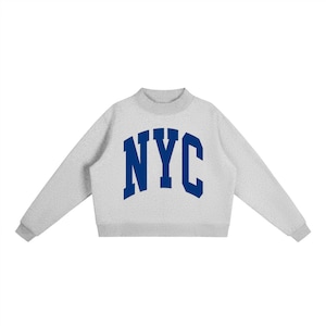 May include: A light gray sweatshirt with the blue letters "NYC" across the chest. The sweatshirt has a mock neck and long sleeves. The cuffs and neckline are a darker gray.