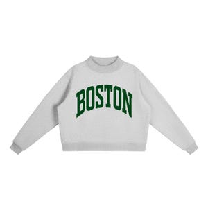 Op de afbeelding: Een lichtgrijs sweatshirt met ronde hals, lange mouwen en een geribbelde kraag. Het woord BOSTON staat op de borst gedrukt in een donkergroen, gebogen lettertype in collegestijl. Het kledingstuk heeft een rechte zoom en een textuur.