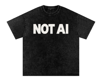 May include: A black short-sleeved t-shirt with a washed, faded texture. The shirt features the text NOT AI printed in large, bold, white capital letters across the centre of the chest. The garment has a crew neckline and a standard boxy fit.