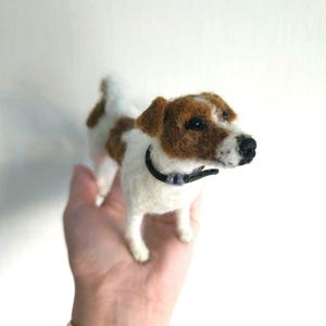 Può includere: Una statuetta di Jack Russell Terrier realizzata in lana infeltrita, con manto bianco e macchie marroni sulla testa e sul dorso. La piccola scultura canina indossa un collare nero, ha occhi scuri e naso nero, con una finitura in lana testurizzata.