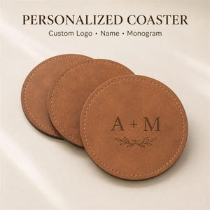 May include: Three round tan coasters with stitched edges. The top coaster features the engraved text A + M above a small leaf design. The image includes the text PERSONALIZED COASTER Custom Logo • Name • Monogram at the top of the frame.