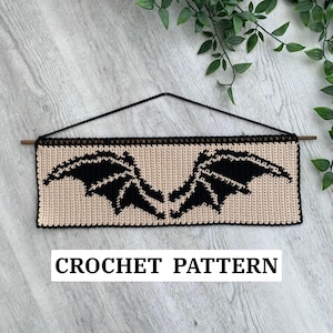 May include: A beige crochet wall hanging with a black bat wing design. The rectangular piece is suspended by a black string and a wooden dowel. The text "CROCHET PATTERN" is displayed at the bottom.