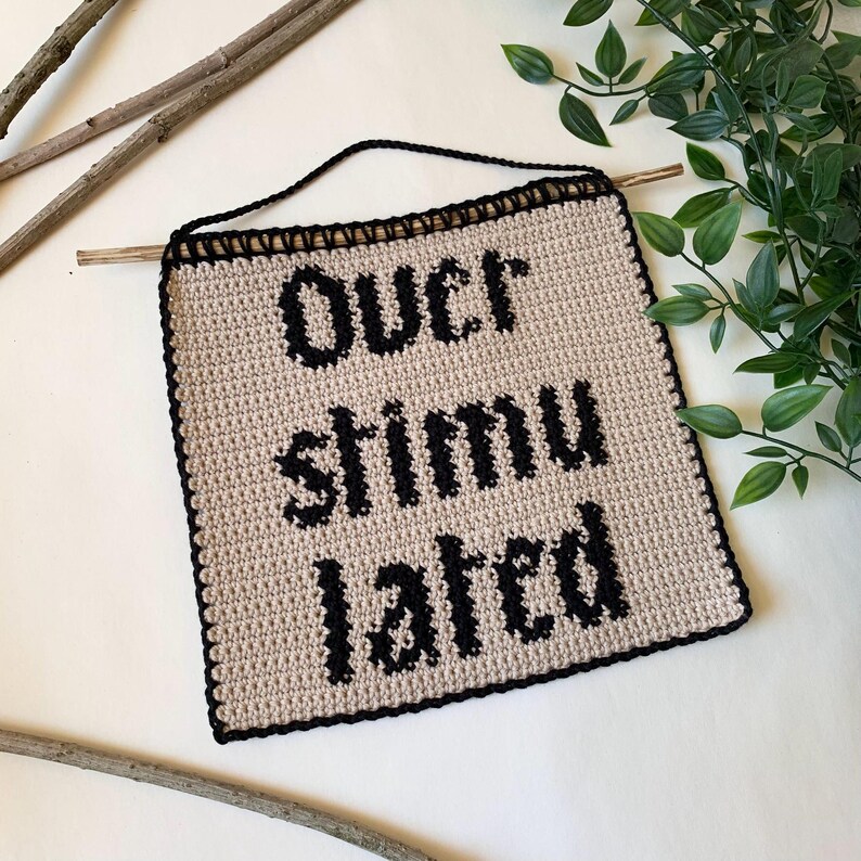 Digital crochet pattern for a wall tapestry featuring the word "Overstimulated" in bold black gothic-style lettering on a beige background. The pattern includes instructions to create the tapestry, which is bordered with black crochet edging. This listing is for the pattern only, not a finished item.