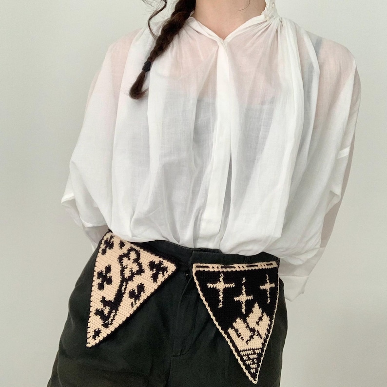 May include: Black shorts with two decorative, triangular crochet patches. One patch is black with a cream-colored design, and the other is cream-colored with a black design. The shorts are paired with a white, semi-sheer blouse.