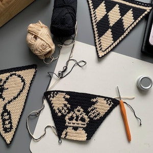 May include: A collection of crochet projects in progress, featuring black and beige yarn. Several triangular pieces with geometric and graphic designs are visible, along with balls of yarn and a crochet hook. The pieces are on a white surface.