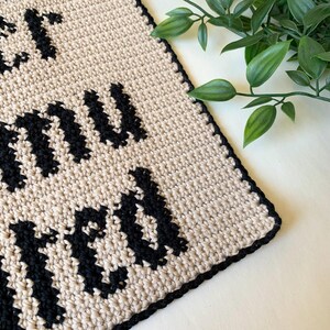 Digital crochet pattern for a wall tapestry featuring the word "Overstimulated" in bold black gothic-style lettering on a beige background. The pattern includes instructions to create the tapestry, which is bordered with black crochet edging. This listing is for the pattern only, not a finished item.