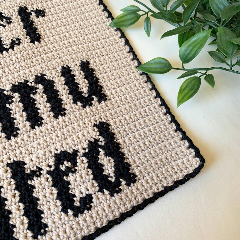 Digital crochet pattern for a wall tapestry featuring the word "Overstimulated" in bold black gothic-style lettering on a beige background. The pattern includes instructions to create the tapestry, which is bordered with black crochet edging. This listing is for the pattern only, not a finished item.