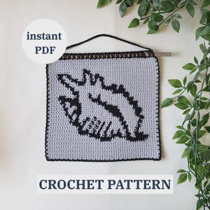 May include: A crocheted wall hanging with a black dinosaur design on a gray background. The text "instant PDF" is in a white circle, and "CROCHET PATTERN" is at the bottom. The hanging is suspended by a black cord.