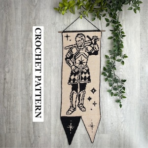 Puede incluir: Un tapiz de pared de ganchillo rectangular con un caballero negro con armadura sobre un fondo beige. El caballero sostiene una espada sobre el hombro. El borde inferior tiene dos puntas, una negra y otra beige, con estrellas. El texto dice CROCHET PATTERN.