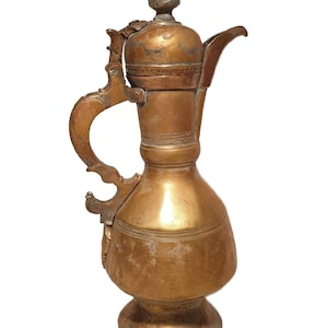 May include: A vintage copper pitcher with a decorative handle and spout. The pitcher has a bulbous body and a lid with a small finial. The copper has a warm, aged patina, suggesting it is an antique or vintage item.