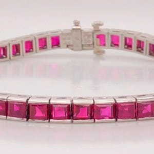 May include: A silver bracelet featuring square-cut, vibrant pink gemstones. The gemstones are set in a row, creating a continuous band. The bracelet has a secure clasp. This piece of jewelry is suitable for special occasions.