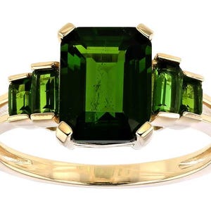 Può includere: Un anello d'oro con una grande pietra verde taglio smeraldo e pietre verdi più piccole. L'anello ha un design a gambo diviso. Le pietre preziose sono incastonate in una fascia d'oro.