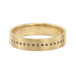 May include: A gold ring with a matte finish. The ring has a row of small, dark gemstones set into the band. The ring is a simple band design, suitable for everyday wear.
