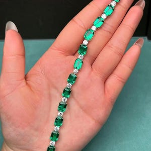 May include: Emerald and diamond bracelet featuring rectangular emerald-cut green gemstones alternating with round, clear diamonds. The bracelet is set in a gold or silver metal, creating a luxurious and elegant look. A beautiful piece of jewelry.