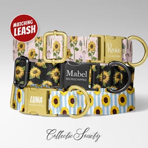 May include: Three dog collars with sunflower patterns. One collar is pink with sunflowers, another is black with sunflowers, and the third is blue and white striped with sunflowers. Each collar has a gold buckle and a name tag.