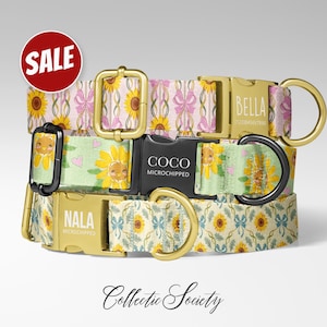 May include: A stack of dog collars with sunflower and bow patterns. The collars have gold-colored buckles and black plastic clasps. One collar has the name "BELLA" engraved, another "COCO", and a third "NALA". A red circle with the word "SALE" is in the upper left.