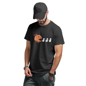 Peut inclure: T-shirt noir avec un motif d'Halloween. Le graphisme comprend une citrouille orange et trois fantômes blancs. Le t-shirt est à manches courtes et porté avec une casquette de baseball noire.