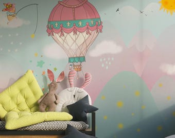 Könnte beinhalten: Ein skurriles Kinderzimmer mit einem Wandbild, das einen Heißluftballon, Berge und eine lächelnde Sonne zeigt. Das Zimmer umfasst ein Bett mit Kissen und Stofftieren, darunter ein Hase und ein sternförmiges Kissen. Die Farbpalette ist weich und pastellfarben.