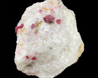 May include: A white mineral specimen with embedded pink crystals. The rough-hewn stone has a crystalline structure, with several small, vibrant pink crystals scattered across its surface. The background is black.