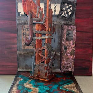May include: A miniature diorama featuring a central orange wooden structure with a large metal hook, a pink locker, and a wall with a sign reading "Af Nee". The base is painted with textured blue, brown, and red patterns, creating a weathered scene.
