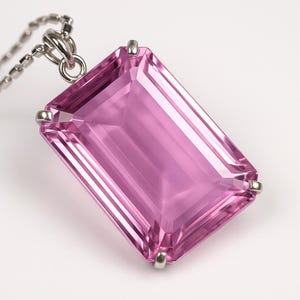 Op de afbeelding: Een rechthoekige, roze edelsteen hanger met een zilveren ketting. De edelsteen heeft een lichtroze kleur en een facetgeslepen slijpvorm. De hanger is gezet in een zilveren metalen zetting.