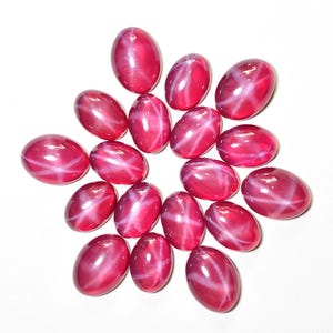 May include: A collection of oval-shaped, deep red gemstones arranged in a circular pattern. Each gem has a prominent white star-like pattern across its surface, creating a striking visual effect against the polished, glossy finish.