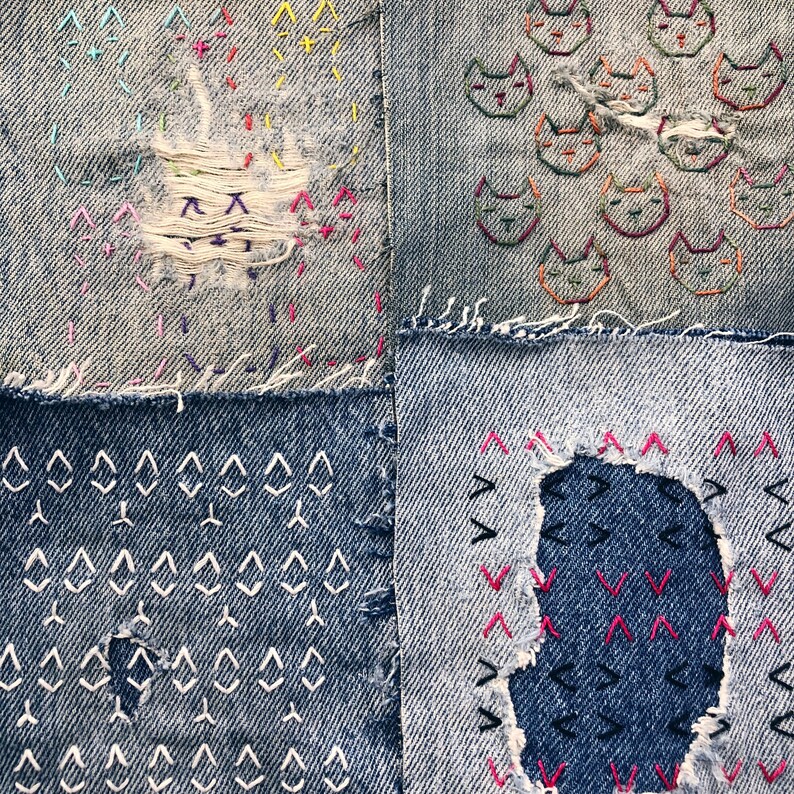 May include: A close-up of a denim patchwork quilt featuring various coloured thread embroidery. The quilt is made from several different pieces of denim fabric, each with a unique pattern. The embroidery is in the shape of cats, triangles, and other geometric shapes.
