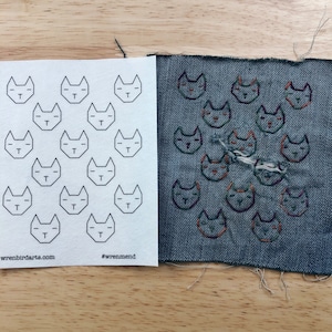 May include: A white sheet of paper with a grid of 15 black cat outlines. Next to it is a piece of blue denim with 15 embroidered cats in various shades of orange, green, and purple.