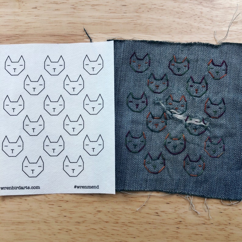 May include: A white sheet of paper with a grid of 15 black cat outlines. Next to it is a piece of blue denim with 15 embroidered cats in various shades of orange, green, and purple.