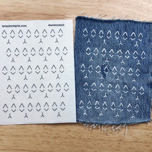 May include: A sheet of paper with a pattern of small triangles printed on it. The paper is next to a piece of blue denim fabric with the same pattern of triangles stitched into it in white thread. The paper has the text "wrenbirdarts.com" and "#wrenmend" printed on it.