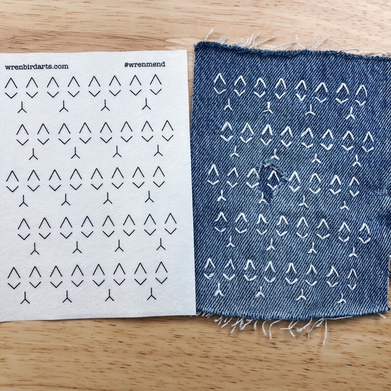 May include: A sheet of paper with a pattern of small triangles printed on it. The paper is next to a piece of blue denim fabric with the same pattern of triangles stitched into it in white thread. The paper has the text "wrenbirdarts.com" and "#wrenmend" printed on it.