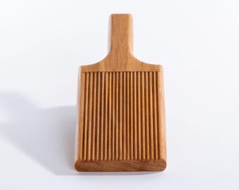May include: A rectangular wooden butter paddle with a handle. The paddle features vertical grooves across its surface. The wood has a warm, natural tone, and the paddle is designed for kitchen use.