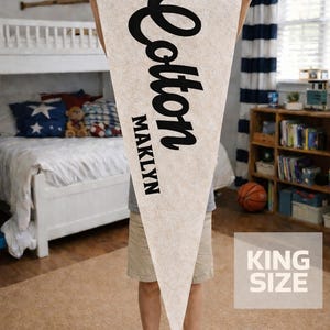 May include: A triangular felt wall banner in an off-white color with a brown top trim. The banner features the black text Cotton in a large script font and the name MAKLYN in a smaller block font. A box in the corner displays KING SIZE.