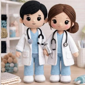 Puede incluir: Dos muñecos de ganchillo hechos a mano vestidos como profesionales médicos. Uno tiene el pelo negro corto, el otro pelo castaño en un moño. Ambos llevan batas blancas sobre uniformes azul claro, estetoscopios negros y uno sostiene una jeringa.